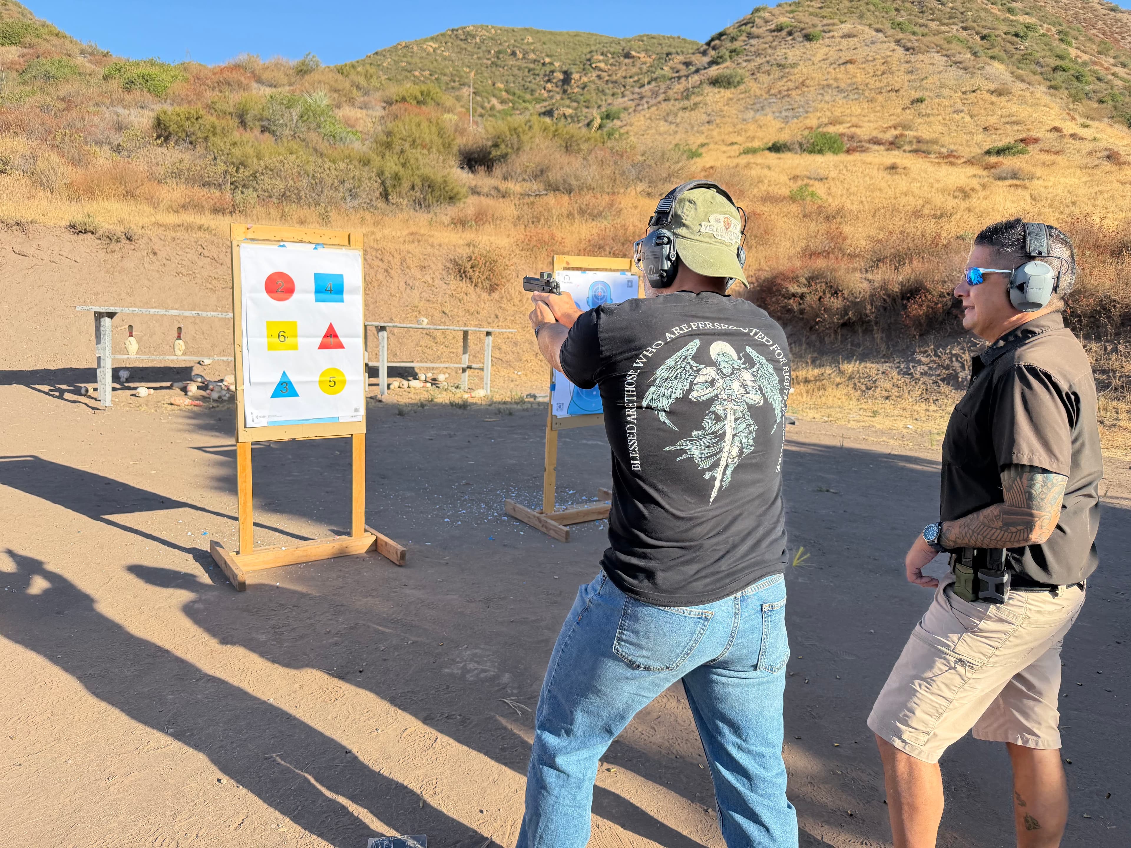 A CTI student is participating in a training drill, aiming at a downrange paper target that has various numbers and colored shapes on it. The CTI instructor is beside him, observing the student's grip, stance, and safe handling skills.